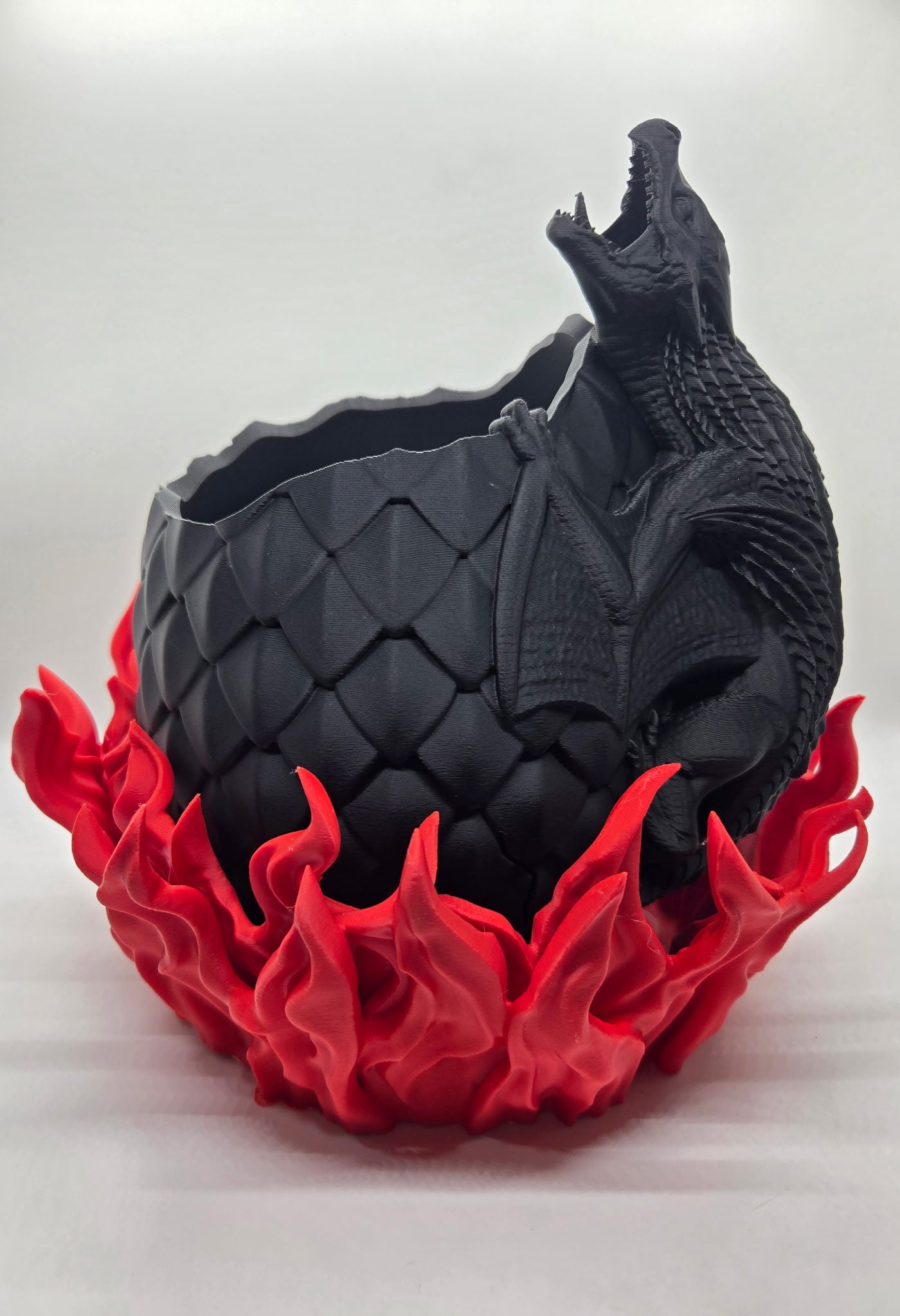 "3D printed dragon egg planter with flame base"

"Fantasy-themed plant pot with dragon coiled around egg"

"Dragon egg flower pot – black egg and red flames"